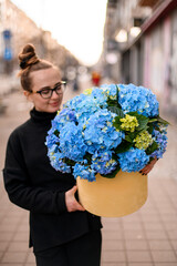 Fototapeta premium Pretty woman holding a large bouquet of blue and yellow hydrangeas