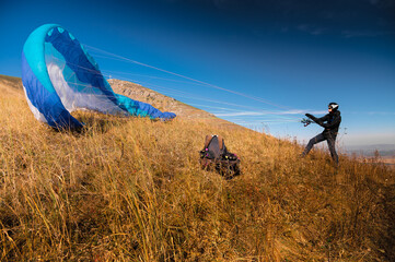The paraglider is preparing to take off. A colorful kite lies on the grass, in the background there...