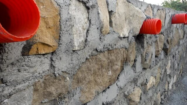 A row of orange culverts or water outlet pipes through a stone retaining wall for storm drainage in the hills of Uttarakhand India.