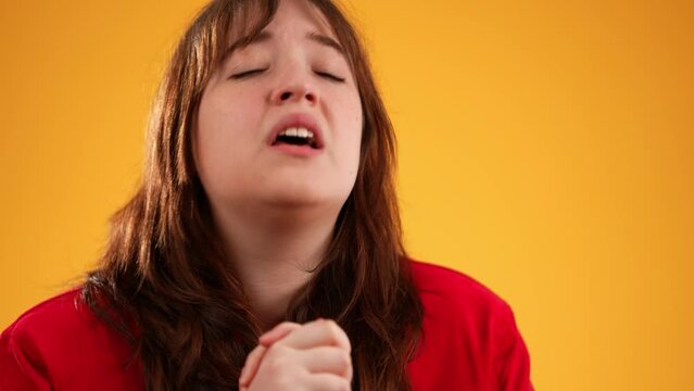 Holding hands folded in prayer begging making wish keep fingers crossed portrait of pretty brunette young woman 20s isolated on yellow background studio with copy space in slow motion