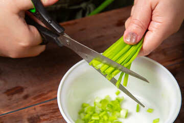 Green onions are cut with scissors into a white salad bowl