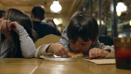 Small Boy Eating Pizza Slice at Restaurant - Child Enjoying Carb-Rich Food at Diner in the Evening
