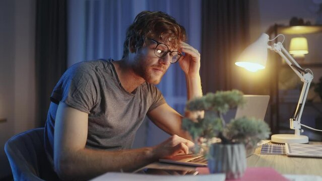 Tired young red hair student or freelancer feel stress during study or work at home workplace at late night Exhausted ginger male with remote distance work or education hard program indoors