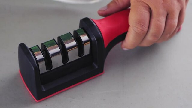 A woman's hand sharpens a kitchen knife in a knife sharpener on the table. Slowmotion