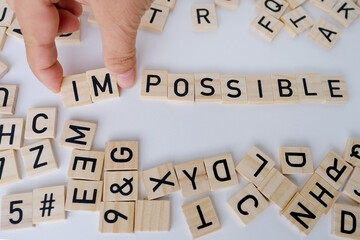 close-up female hand holds square wooden alphabet blocks, word impossible turns into word possible...