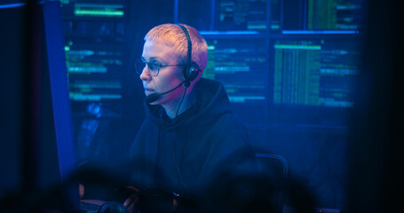 Caucasian woman with short blonde hair and in headset working at computer in call monitoring center...