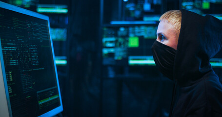 Side view on female Caucasian hacker with masked face working on computer and browsing for data...
