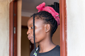young african girl with braids standing in the door of the house