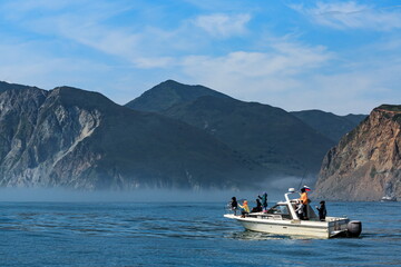 Fishermen sail on a boat against the backdrop of large mountains on the Pacific Ocean, clear sunny day, Kamchatka.