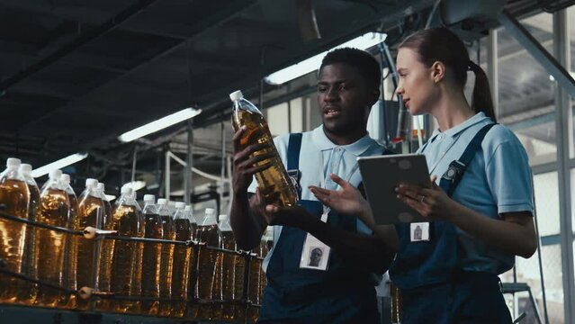 Medium stab footage of two manufacturing engineers discussing quality of new soda production line, smiling and typing information into tablet at beverage plantMedium stab footage of two manufacturing 