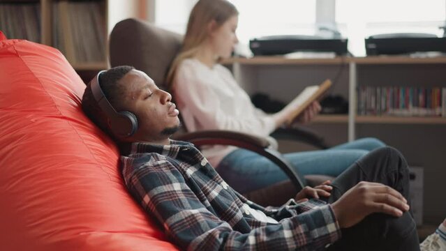 Man listens to audio via earphones in library
