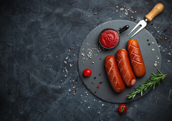 Grilled sausages with herbs, incisions, on slate stone plate round, dark background