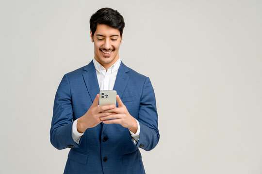 A young businessman in a tailored blue suit uses his smartphone, displaying a moment of connectivity and accessibility in the business realm standing isolated on white