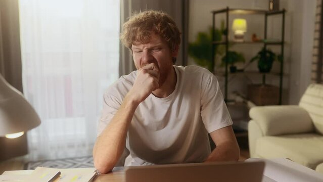 Handsome young red haired man working on laptop computer having distance remote work or study and eating fresh red apple at home workplace Healthy food concept