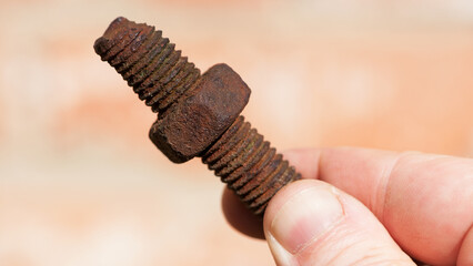 old rusty bolt, iron rod with screw threads, in hand. Rusted mechanical components. holding...