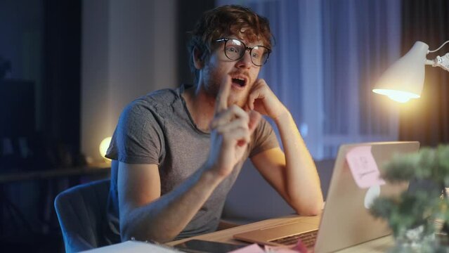Handsome red haired man student or freelancer thinks questioningly and finding solution and typing on laptop computer at home at late night Idea pointing forward index finger concept