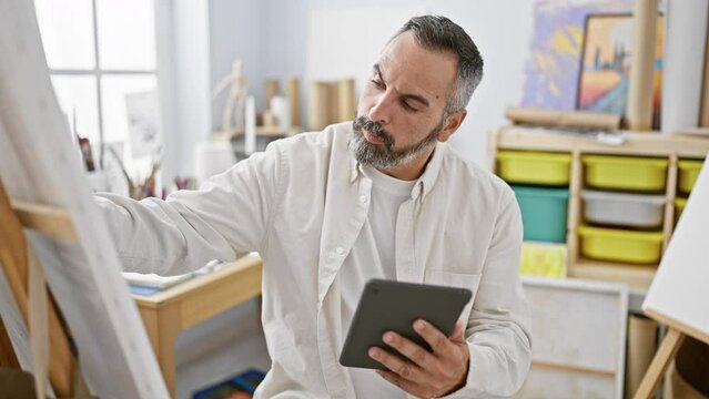 Mature artist man with beard and grey hair using tablet in art studio