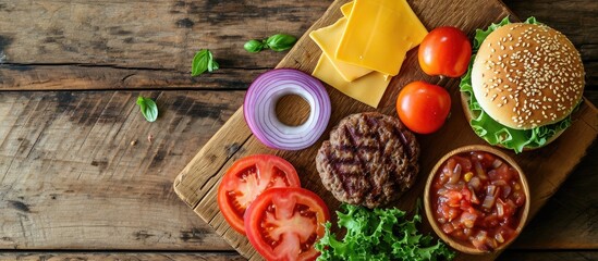 Beef burger ingredients on a wooden board with a place for text shot from above Grilled patty lettuce leaf tomato Cheddar cheese onion and a sesame bun. Copy space image