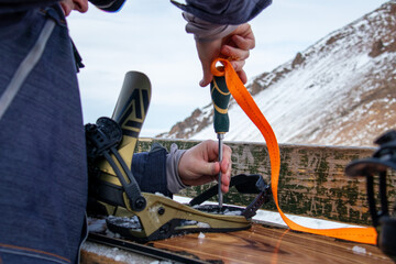 A guy twists a snowboard attachment with a screwdriver at a ski resort