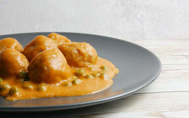 Appetizing homemade dish of meatballs, with tomato sauce and peas, on the table.