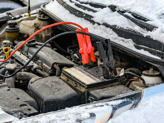 Charging automobile discharged battery by booster jumper cables at winter. Close-up. Problem...