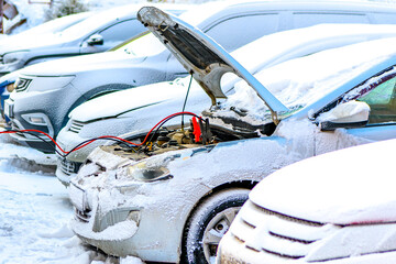 Charging automobile discharged battery by booster jumper cables at winter. Close-up. Problem...