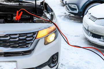 Charging automobile discharged battery by booster jumper cables at winter. Close-up. Problem...