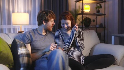 Amazed red haired family extremely happy after read message on smartphone at home Excited couple pleased rejoices received great successful news or result at late night indoors