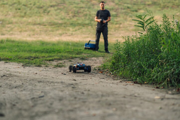 Man in blurry background running a remote control car in nature.