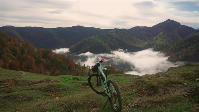 Electric bike stands on high mountain above clouds in autumn in Bavarian Alps. Brightly colored mountain e bike against German alps in higher than clouds. Theme travels in alpine by eletro cycle. 
