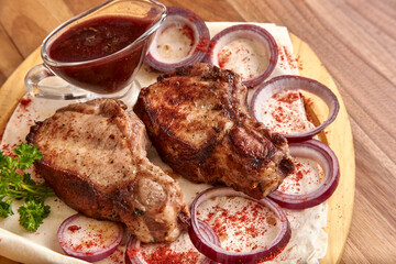 Part of the wooden board with fried beef meat with red onion rings, sauce and pita bread on the wooden table, close-up perspective view, shallow depth of field. Meat and onion in focus