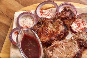 Part of the wooden board with fried beef meat with red onion rings, sauce and pita bread on the wooden table, close-up perspective view, shallow depth of field. Meat and onion in focus