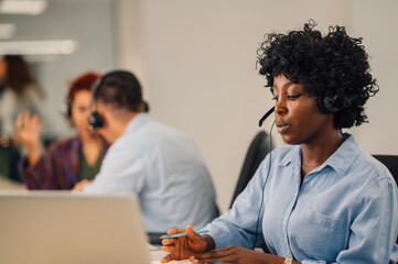 African american woman with headset working in an office and using a laptop