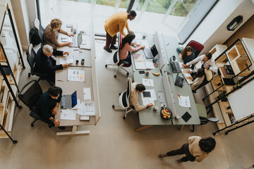 Fototapeta premium Top angle view photo of employees collaborating indoors, discussing and sharing ideas. Productive and creative teamwork in a successful workplace.