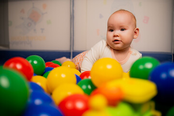 Cute baby girl playing with colorful balls in kindergarten.