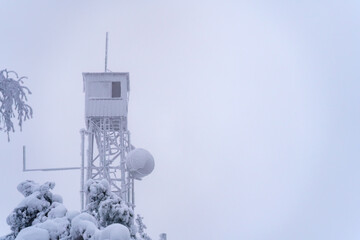 Frozen fire tower against white overcast sky in winter.