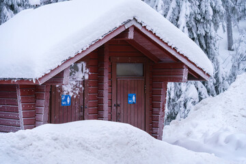 Red wooden toilet building covered in snow.