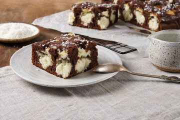 piece of chocolate cake on a plate. Chocolate and coconut cake on a white wooden background