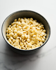 White chocolate drops in the bowl on white marble background. Baking ingredient