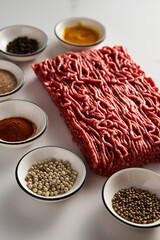 Raw and Fresh Minced Beef on white marble background with spices for cooking. Minimalistic food photo, high-key.
