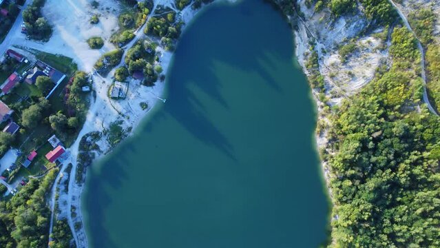 Aerial view from above on turquoise lake in an old quarry, around the road houses and trees