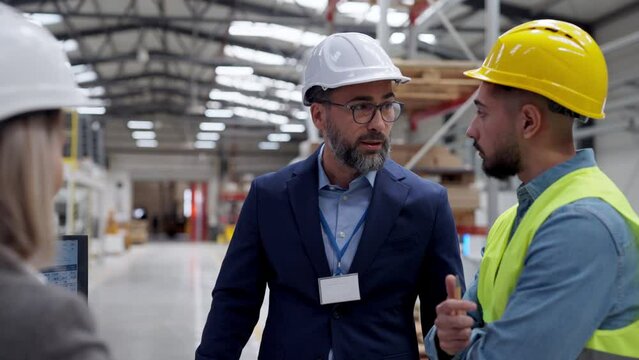 Engineers consulting with director in modern industrial factory, talking about new production project or investment. Team management in manufacturing facility.