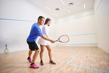 Man instructor guides woman emphasizing precise squash hitting techniques