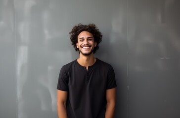 Portrait of young latin man with curly hair smiling against grey background