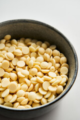 White chocolate drops in the bowl on white marble background. Baking ingredient