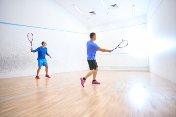 Active sporty men training together on squash court