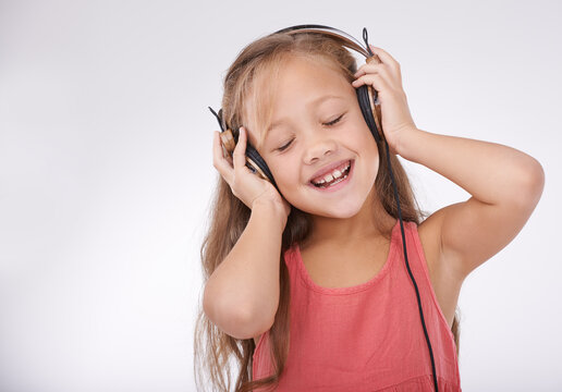 Girl kid, music and happy with headphones in studio for audio, subscription and streaming multimedia on white background. Child, smile and listening to podcast, hearing sound and radio connection