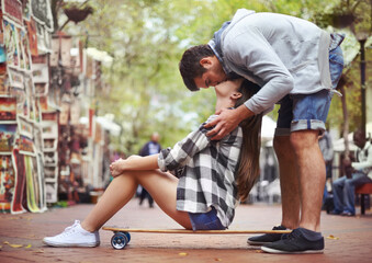 Couple, sitting on skateboard and kiss in city, happy and romantic partner, learn together and relationship. Cape town, fun and hobby with boyfriend and girlfriend in street, love and dating
