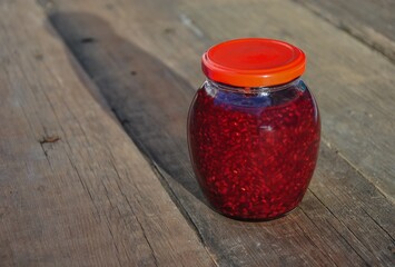 glass jar with raspberry jam on a wooden table. a jar of homemade raspberry jam.