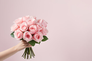 Hand holding a rose bouquet on a pink background. Copy space